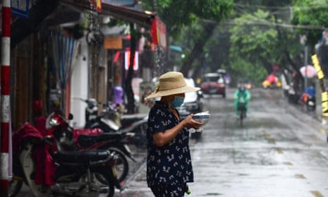 A woman carries a bowl of pho across the street in the rain in Hanoi 