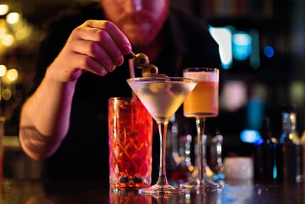 A bartender puts olives into a martini and a trendy bar