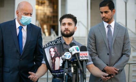 A man speaking into a mike flanked by two other men wearing suits