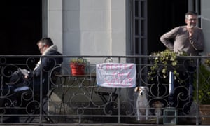 Two men stand on their balcony where hangs a banner reading stay at home, in Nantes, France