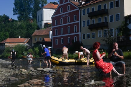 People sit on chairs in the river while others manoeuvre a small plastic boat