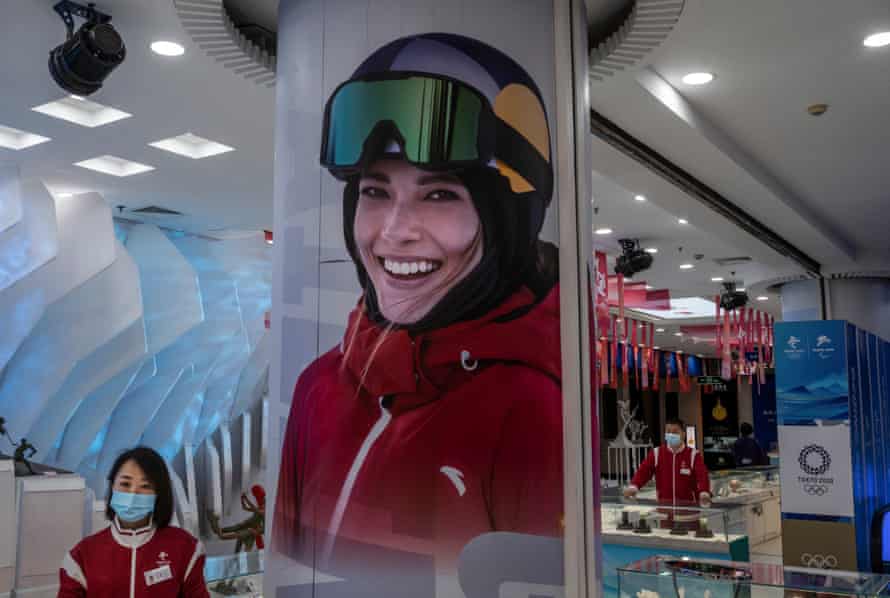 Plakat z chorym Gu jest widoczny obok sklepikarza w oficjalnym sklepie z towarami na Zimowe Igrzyska Olimpijskie w Pekinie 2022 w dzielnicy handlowej Wangfujing w Pekinie.