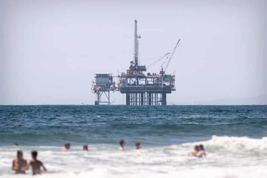 People swim in the Pacific Ocean next to the Huntington beach pier in front of an offshore oil rig in Huntington Beach, California.