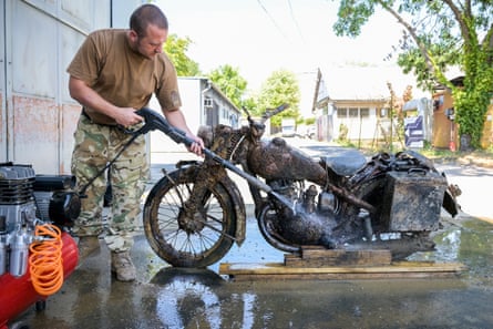 Man in military clothing uses a pressure washer to clean rust off the recovered motorcycle