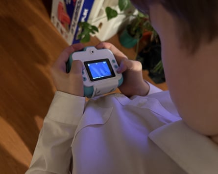A child examines a small handheld digital camera with a glowing blue screen