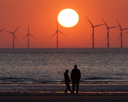 Offshore wind turbines photographed from land. The sun is setting against an orange sky