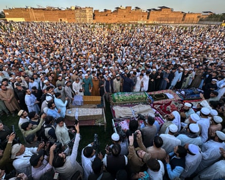 A vast crowd in a square gather around several coffins