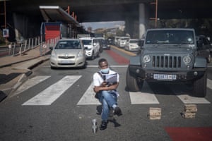 A man sits on bricks pretending to read as student members of the African National Congress and the Economic Freedom Fighters block traffic in Braamfontein