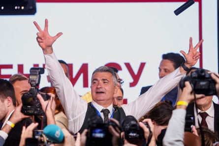 Ilija Srdanović raises both arms making peace signs, smiling, surrounded by photographers