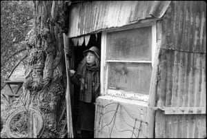 A woman looks out of a corrugated iron shelter