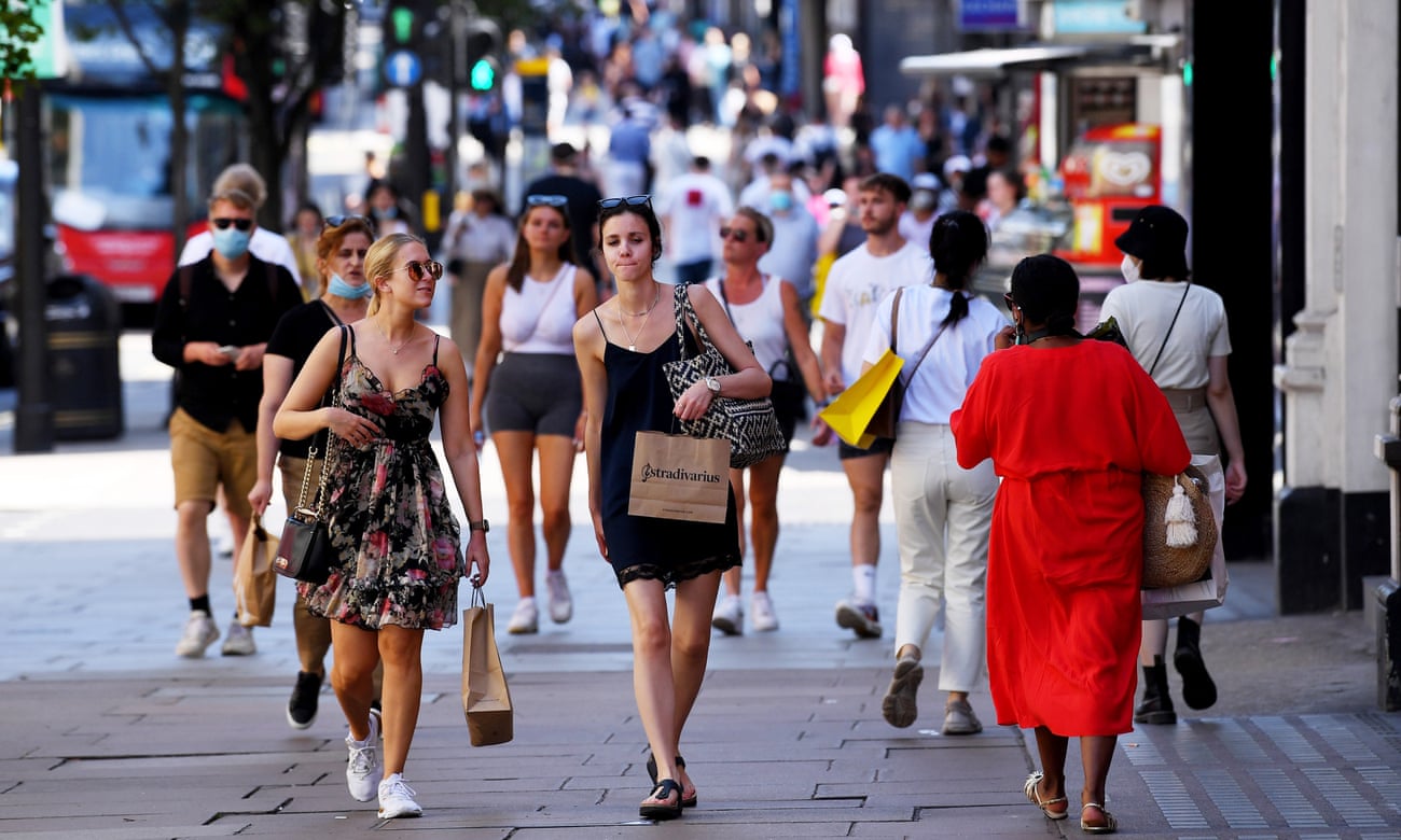 Shoppers on Oxford Street in London, some in masks, with the sun shining