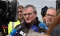 The prefect of Pas-de-Calais, Jacques Billant, updates reporters on the incident. He is a middle-aged man wearing spectacles, surrounded by reporters' microphones