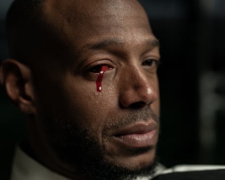 A film still from Him of Marlon Wayans as Isaiah. He is looking at the camera, with a drop of blood running from his right eye.