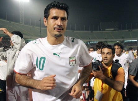 The striker Ali Daei in 2006, wearing white Iran kit with green detail, with a photographer behind him.