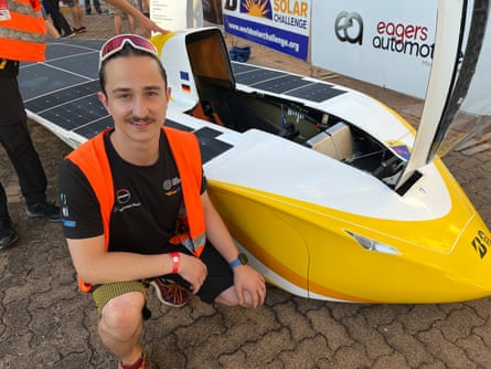 A driver from Germany kneels beside his sleek, yellow and white solar powered race car