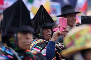 A person wearing traditional Bolivian costume, including black triangular-shaped headwear, takes a photo with a phone