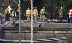 Workers stand on a damaged railroad bridge on Tuesday at the scene of the crash.