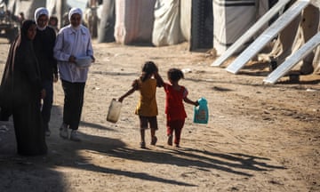 Two children walk along a dusty path carrying water containers