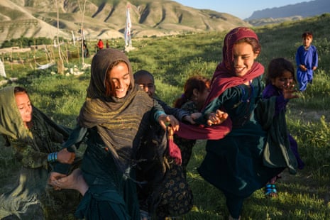 A group of girls in headscarves laugh as they run and play in a field.
