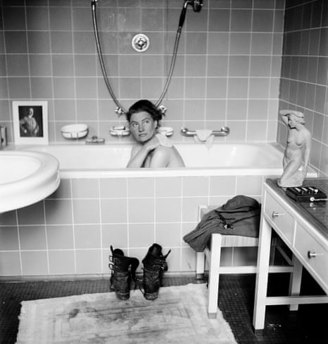 Lee Miller in Hitler’s bathtub, Hitler’s apartment, Munich, Germany 1945 by Lee Miller with David E Sherman, showing combat boots on the bath mat stained with the dust of Dachau; and a photograph of the previous owner of the flat propped on the edge of the tub