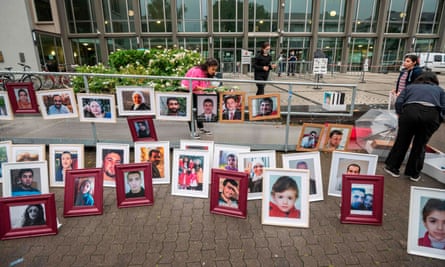 A woman arranges framed photos of people, including young children. on the pavement outside the court