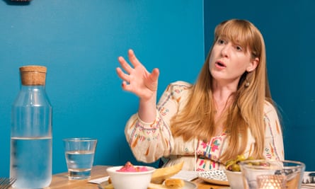 A woman sitting talking at a restaurant table in front of a blue wall