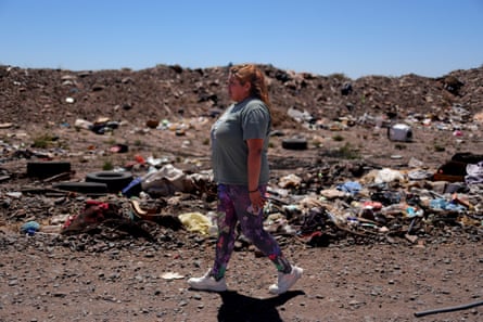 A woman walks past rubbish strewn on the ground, with mounds of dirt and rubbish in the background.