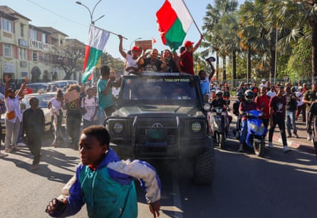 A boy runs in front of a pickup truck on which people are waving flags from