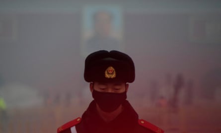 A paramilitary police officer wearing a mask stands guard in front of a portrait of the late Chairman Mao during smog at Tiananmen Square in Beijing