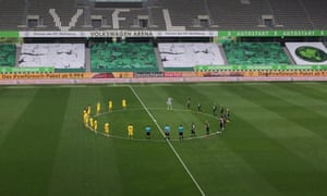 Dortmund and Wolfsburg players stand on the centre circle for a minute of silence for the victims of COVID-19.