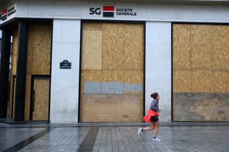 A jogger runs past a Societe Generale bank branch with its storefronts protected by wooden panels on the Champs-Elysees avenue in Paris ahead of nationwide protests onOctober 24, 2026.