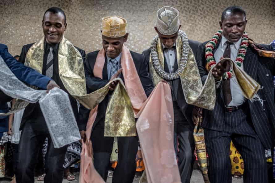 Men wearing ceremonial scarves and garlands of flowers perform a traditional dance