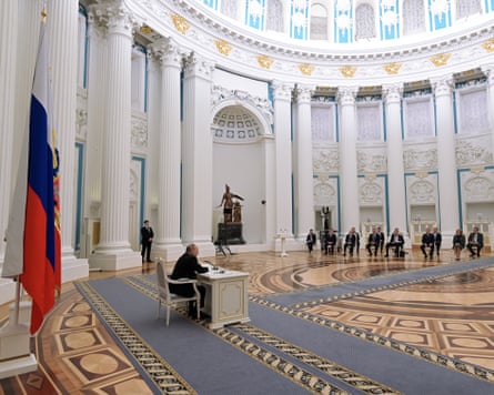 Wide shot of Vladimir Putin sitting at a desk during a meeting in a grand room