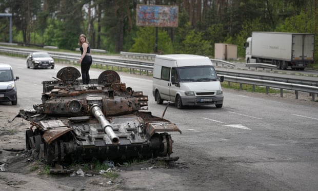A woman stands on a destroyed Russian tank on the main highway into Kyiv on Friday