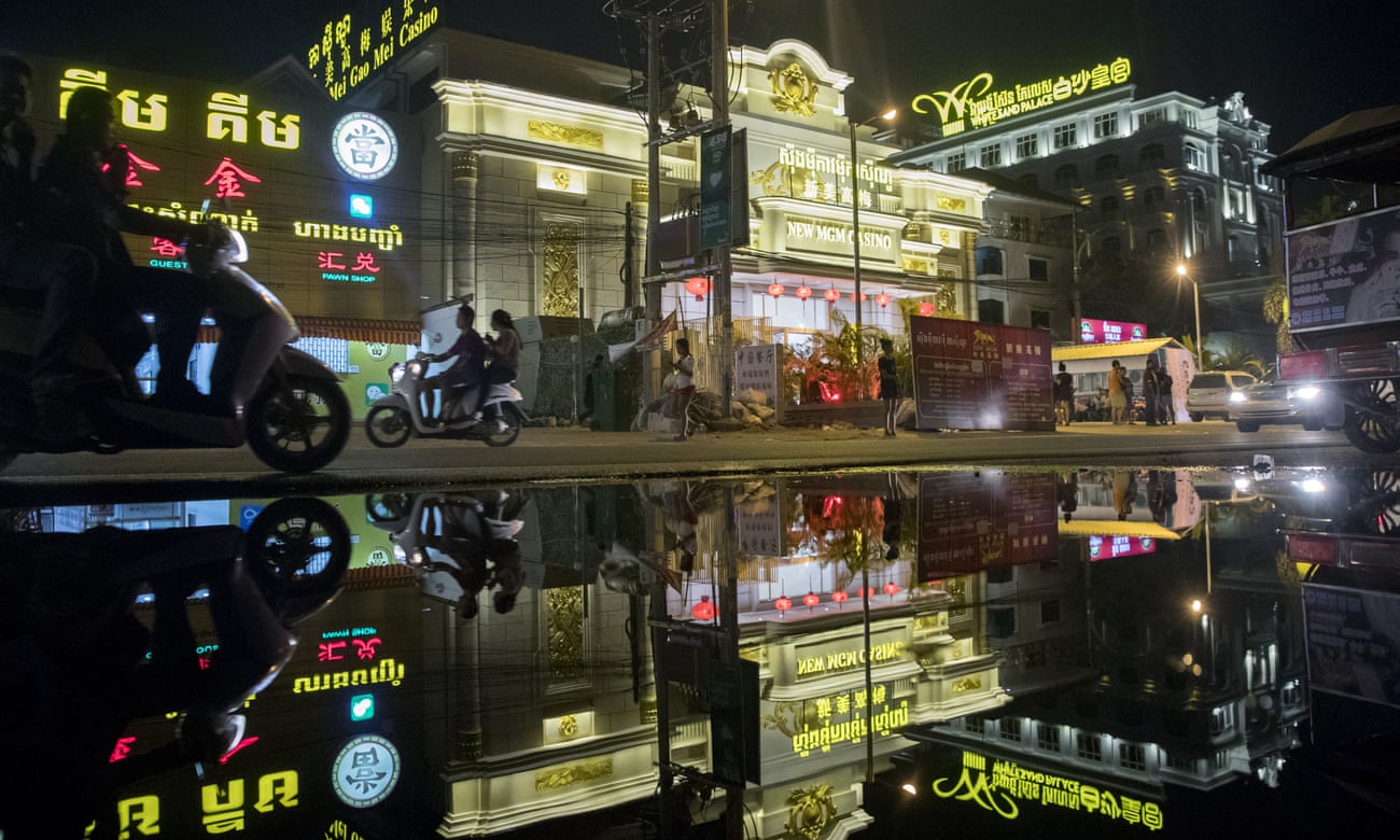 Motorcyclists and the New Mei Gao Mei (New MGM) casino are reflected in a puddle at night in Sihanoukville, Cambodia