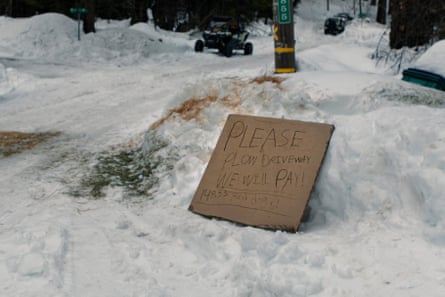 A hand-drawn cardboard sign stuck in the snow reads ‘Please plow driveway. We will pay!’