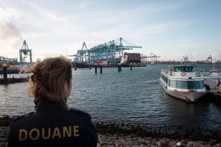 A customs officer with her back to camera looks out over the Dutch port of Rotterdam