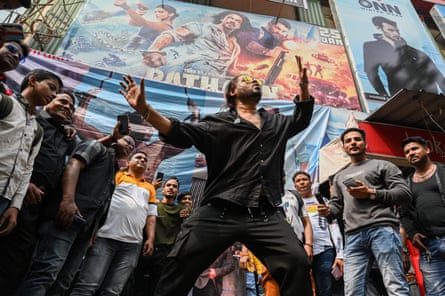 Bollywood superstar Shah Rukh Khan dances with others around him under film poster.