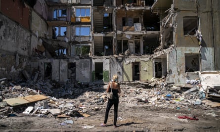 A woman stands in front of a badly damaged apartment block which has had its entire facade blown away