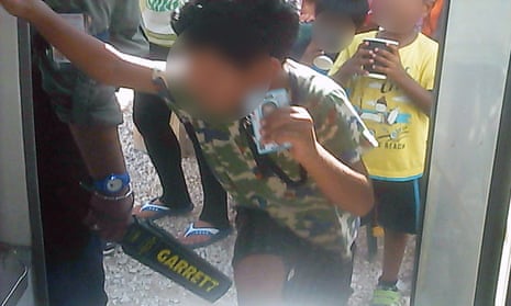 An asylum seeker boy on Nauru holds up his ID card as a guard searches him