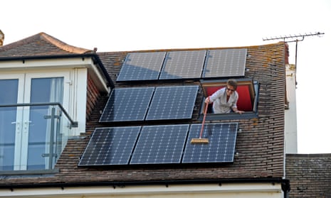 Woman brushing off dust from solar panels on roof of her home in Sussex