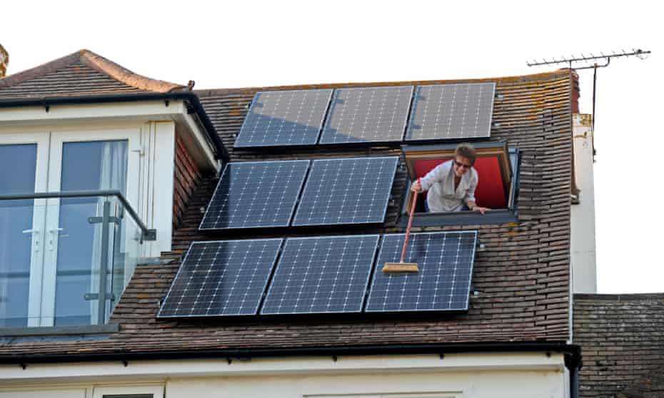 A woman sweeps dust from solar panels on the roof of her home in Sussex.