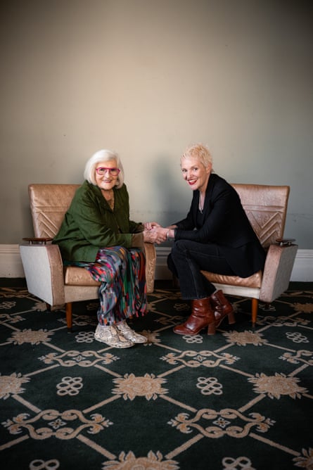 Comedian Liz Hicklin and Jacinta Parsons sit on chairs holding hands