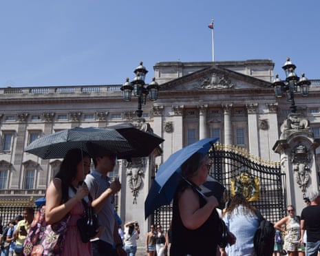 People shelter under umbrellas from the scorching sun outside Buckingham Palace in London.