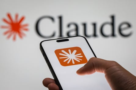 Claude name and logo on a large screen behind a smartphone that features the same logo