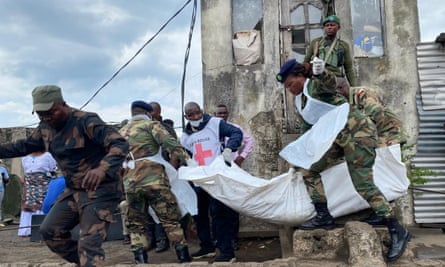 Soldiers on a quayside and a man in a Red Cross tabard carrying a corpse in a white bodybag