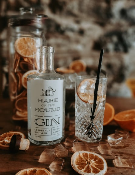 A bottle of gin with ‘Hare of the Hound’ printed on the bottle. A glass with an orange slice and a black straw is next to it