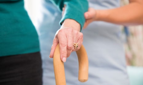 An elderly woman's hand on a walking stick with a care worker supporting her arm