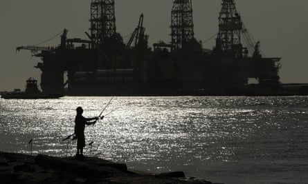 A man fishes near docked oil drilling platforms