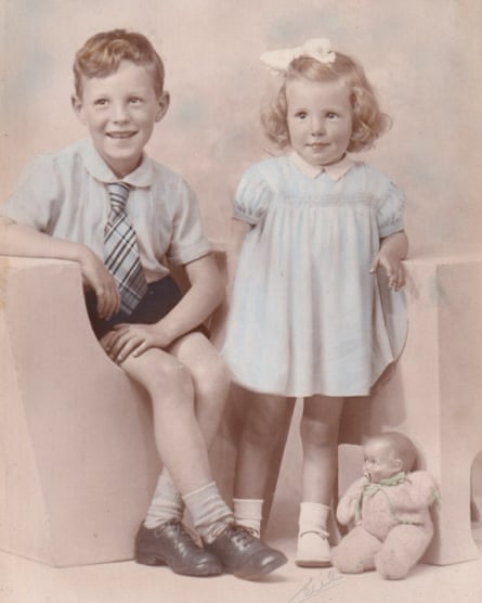 A six-year-old boy wearing a shirt and tie and a girl with a smock dress and a white bow in her hair. A baby doll is on the floor next to them.